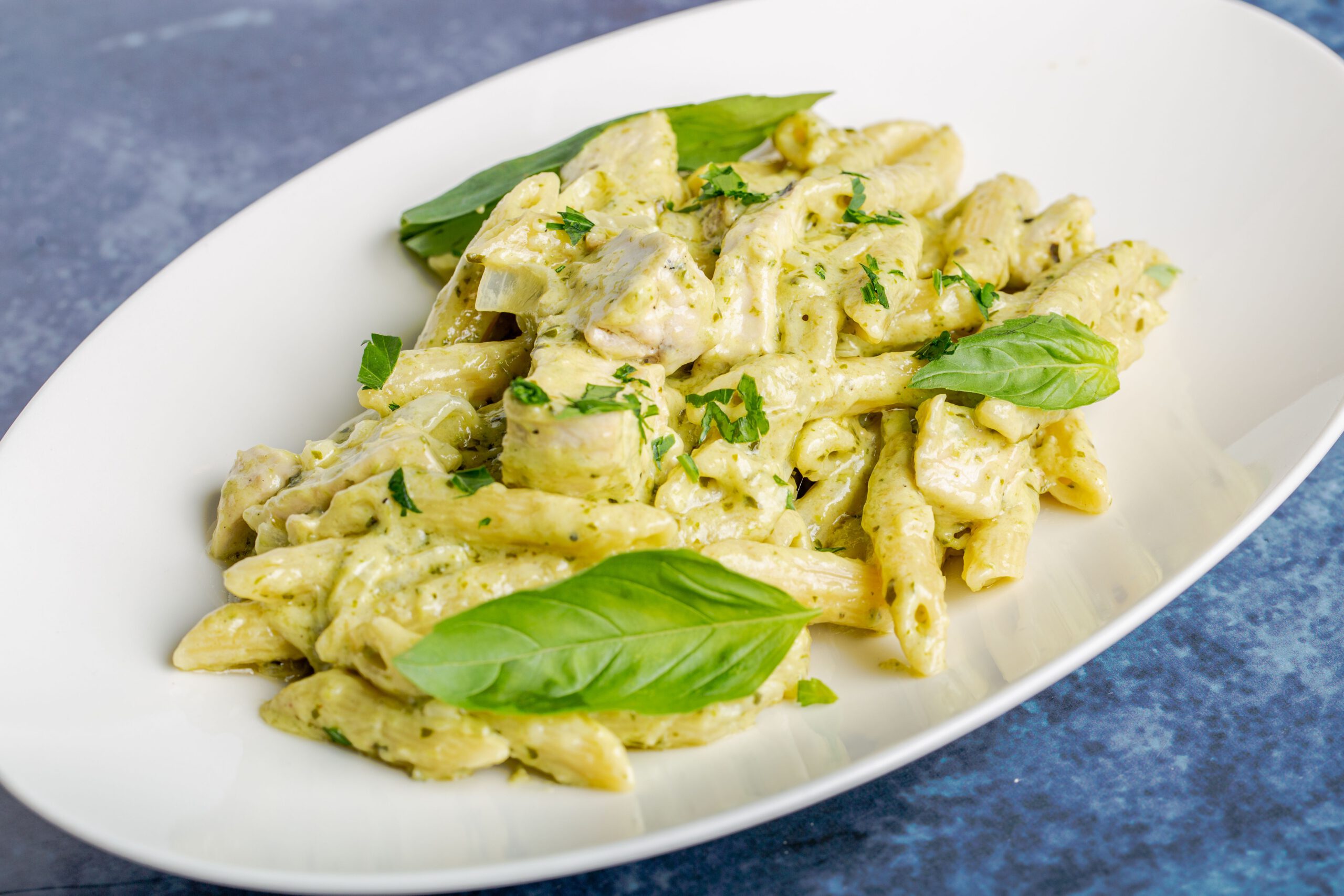 Closeup shot of penne pasta with chicken, cheesy sauce and basil on a flat plate